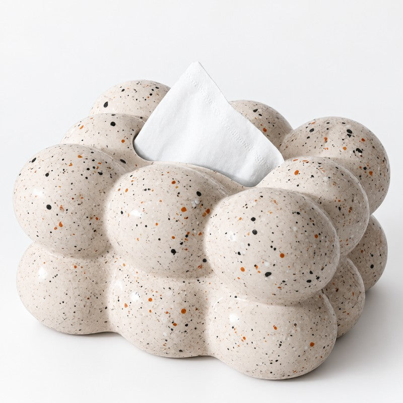 Close-up of a bubble-shaped tissue box in speckled beige with black and brown flecks, a white tissue emerging from the top.