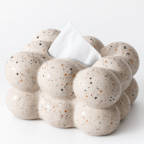 Close-up of a bubble-shaped tissue box in speckled beige with black and brown flecks, a white tissue emerging from the top.