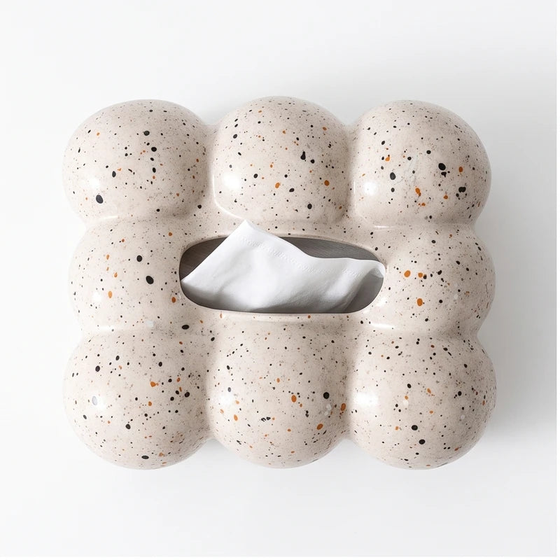 Light beige ceramic tissue box with a bubbly, rounded shape and speckled black and orange spots, dispensing a white tissue.