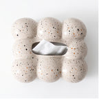 Light beige ceramic tissue box with a bubbly, rounded shape and speckled black and orange spots, dispensing a white tissue.