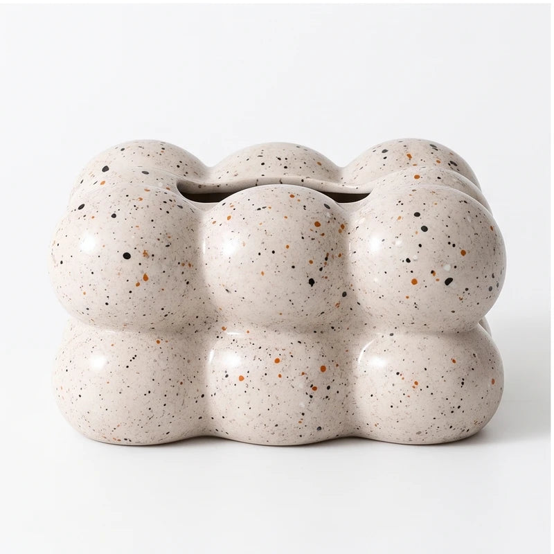 Beige ceramic holder with a bubbly, cloud-like shape and speckled black and brown accents on a white background.
