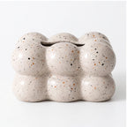 Beige ceramic holder with a bubbly, cloud-like shape and speckled black and brown accents on a white background.