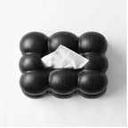 Black bubble-textured tissue box with a single white tissue peeking from the top opening, against a white background.