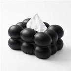 Black bubble-textured tissue box with a single white tissue protruding from the top, against a white background.