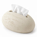 Light beige, pebble-shaped tissue holder with a rough, textured finish and a white tissue emerging from the top slot.