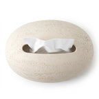 Light beige oval tissue dispenser with a textured surface, featuring a slot from which a white tissue protrudes.