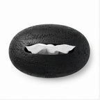 Black oval tissue box with a rough, textured surface and white tissues pulled partly from its central opening.