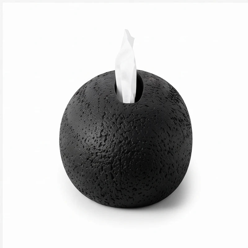 Spherical black textured dispenser with a white tissue emerging from a narrow slot on its top, isolated on white.